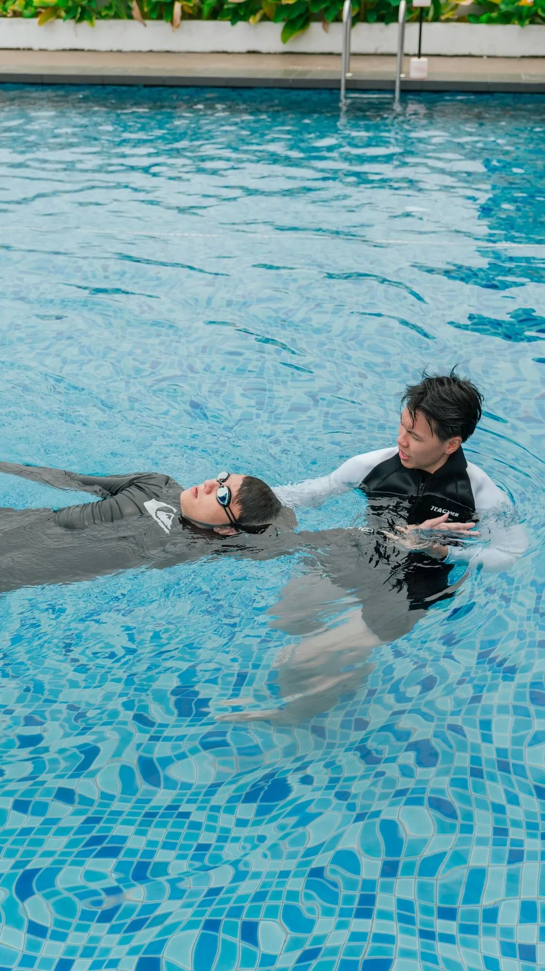 A Swimwerks coach supporting a swimmer floating on her back in a condo pool