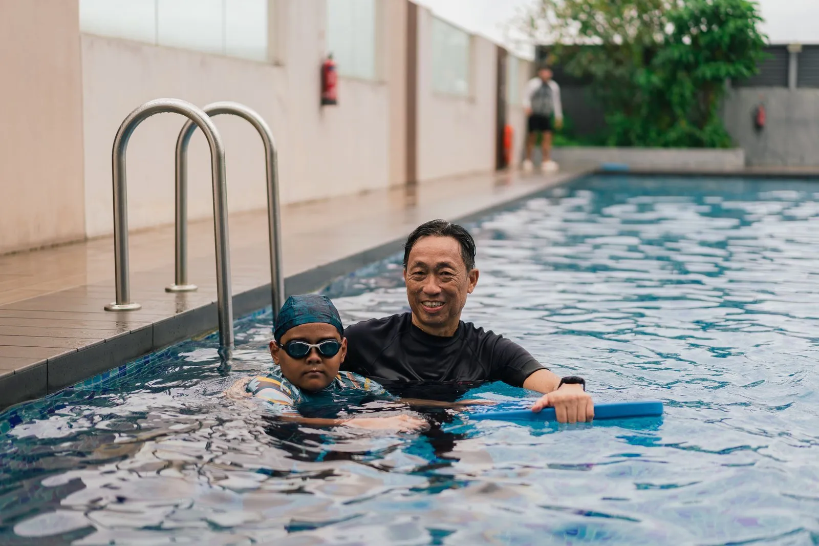 A smiling coach in the water teaching a child with a kickboard