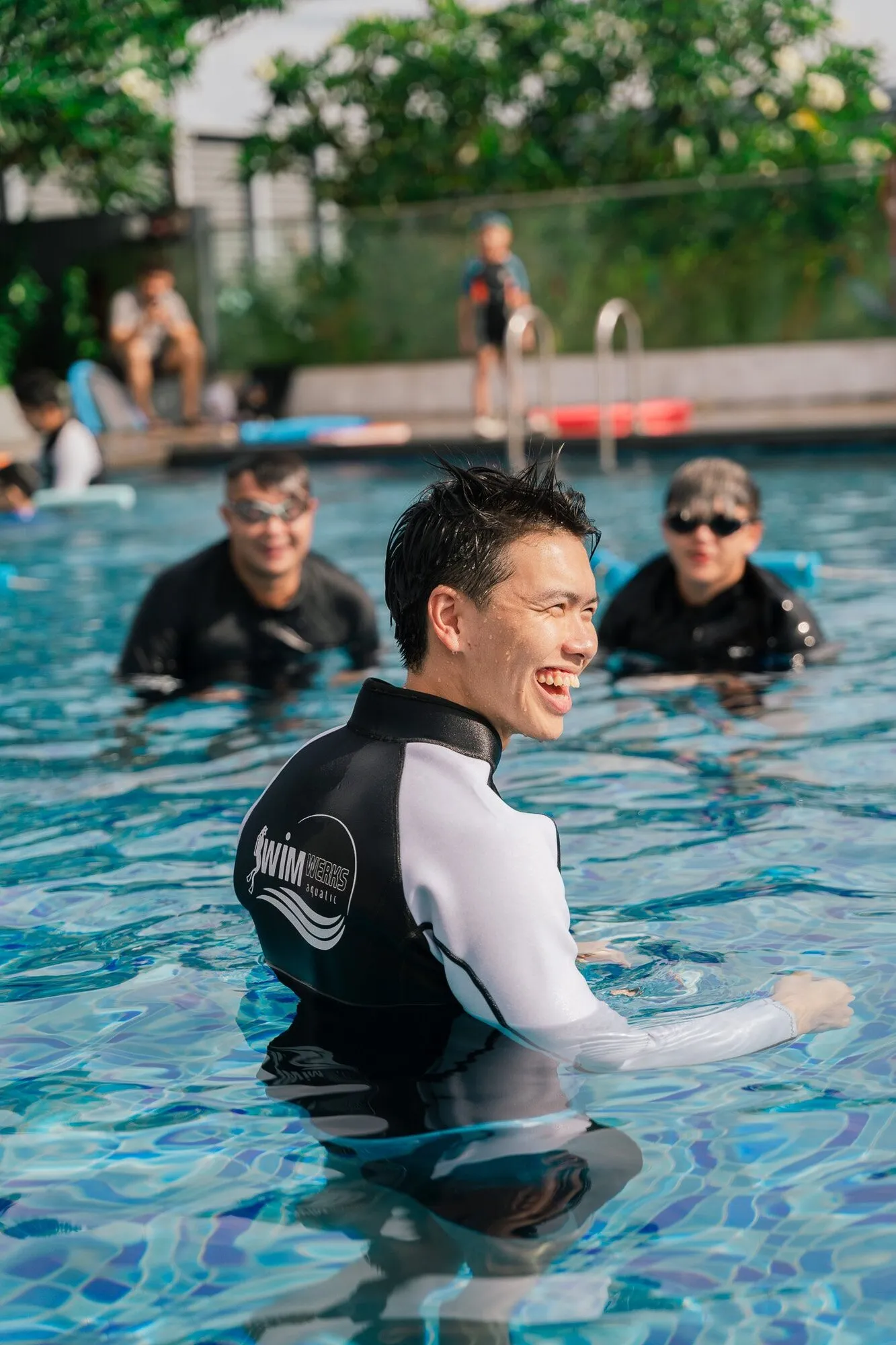 A smiling coach trainer in the pool with trainee coaches behind him