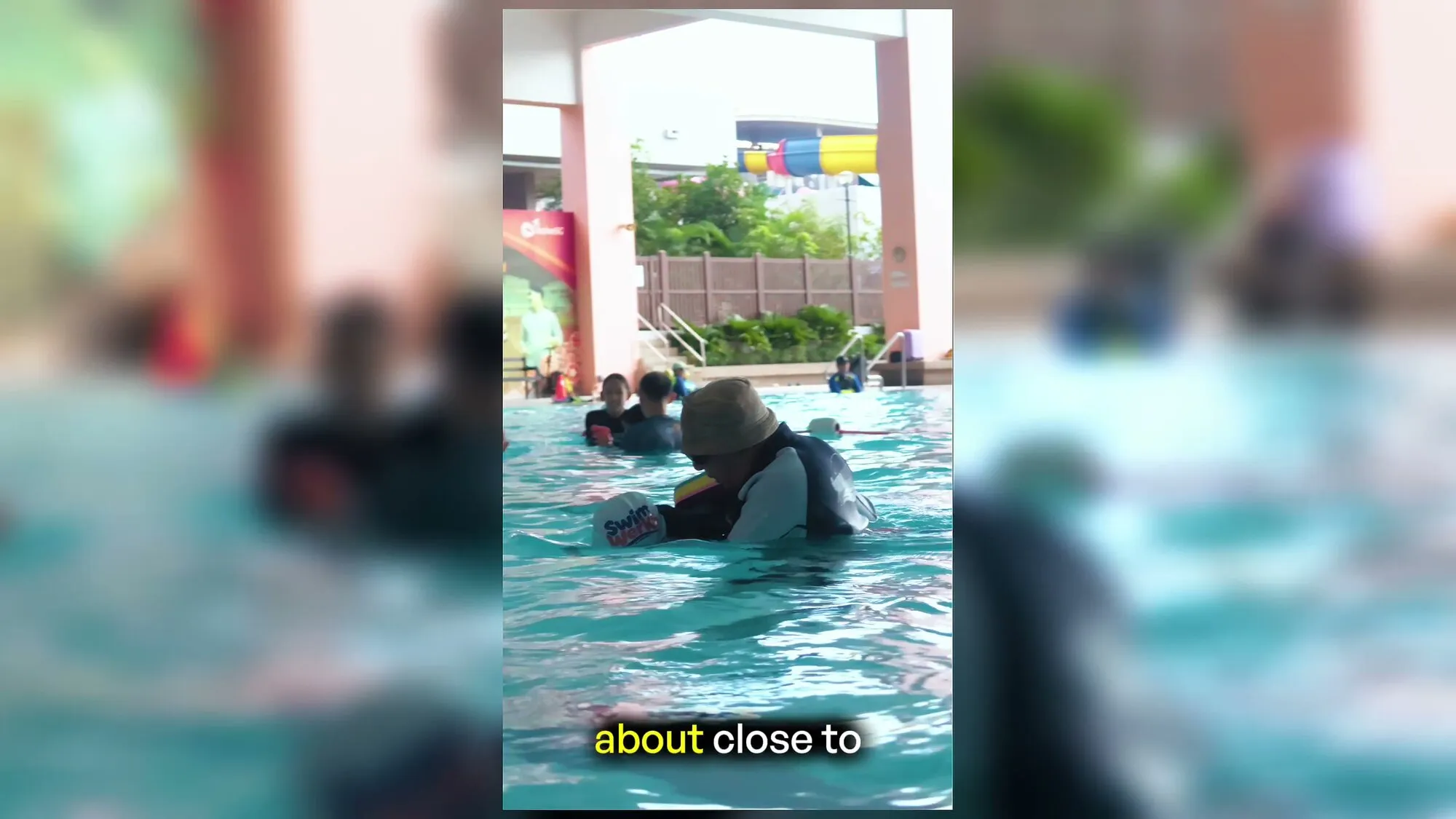 Teacher Richard, in a bucket hat, speaking beside a public pool
