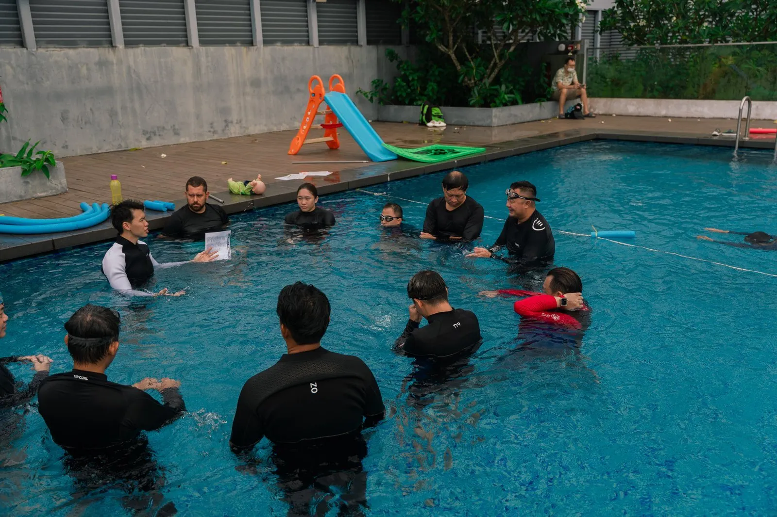A group of trainee coaches standing in the pool around an instructor
